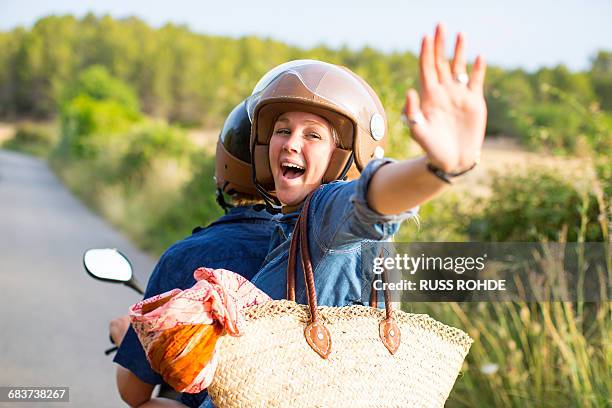 young woman riding pillion on rural road waving, majorca, spain - moped stock-fotos und bilder