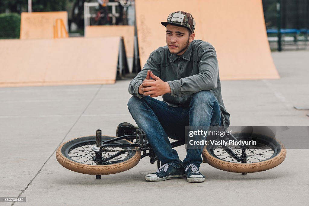 Teenage boy contemplating while sitting on bicycle at skateboard park