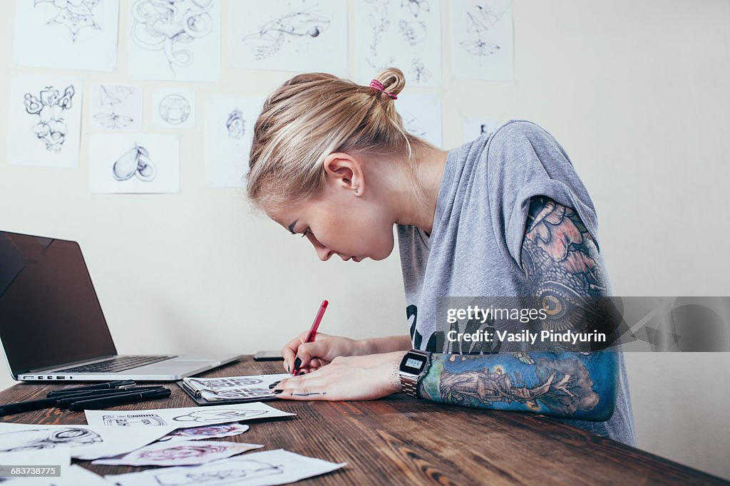 Confident tattoo artist working on designs by laptop at art studio