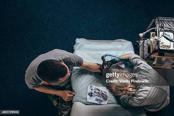 high angle view of tattoo artist tattooing on human hand at studio - tattooing stock pictures, royalty-free photos & images