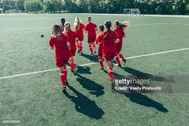rear view of soccer players running on field - woman football stock-fotos und bilder