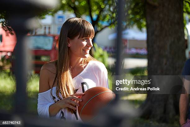 young woman outdoors, holding basketball, smiling - andreas pollok stock-fotos und bilder