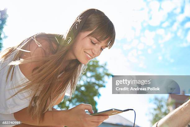 young woman outdoors, using smartphone, smiling - andreas pollok stock-fotos und bilder