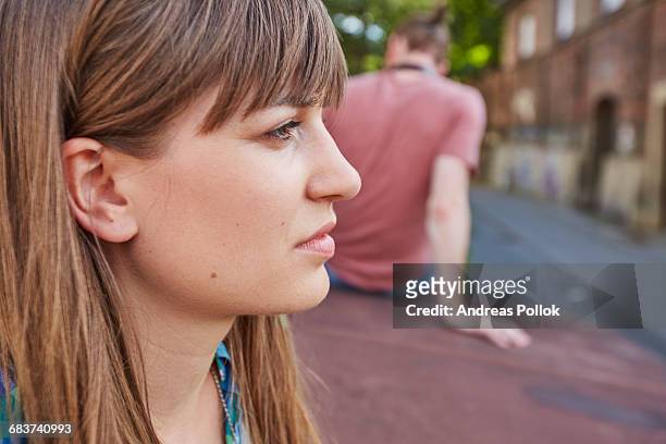 young couple outdoors, sitting away from each other, sad expression on young womans face - andreas pollok stock-fotos und bilder