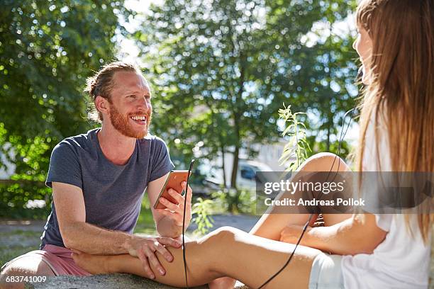 young couple outdoors, listening to music through earphones - andreas pollok stock-fotos und bilder