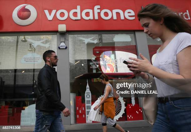 Pedestrians walk past a Vodafone store in central London on May 16, 2017. - Vodafone logged today a large annual net loss after slashing the value of...