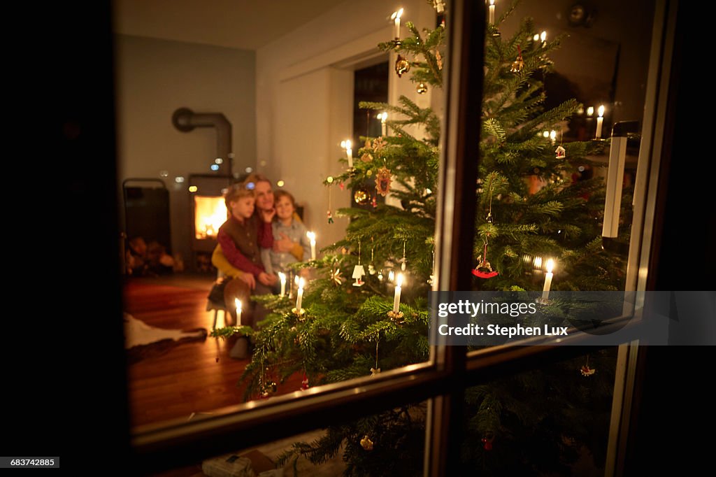 Mother and sons sitting at home at Christmas, looking at illuminated Christmas tree