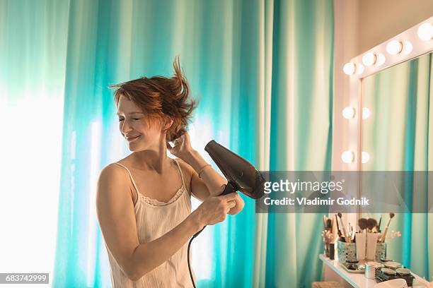 smiling woman standing in front of mirror at dressing table - drying hair stock-fotos und bilder