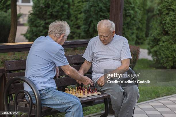 senior friends playing chess while sitting on park bench against trees - 85 2016 stock pictures, royalty-free photos & images