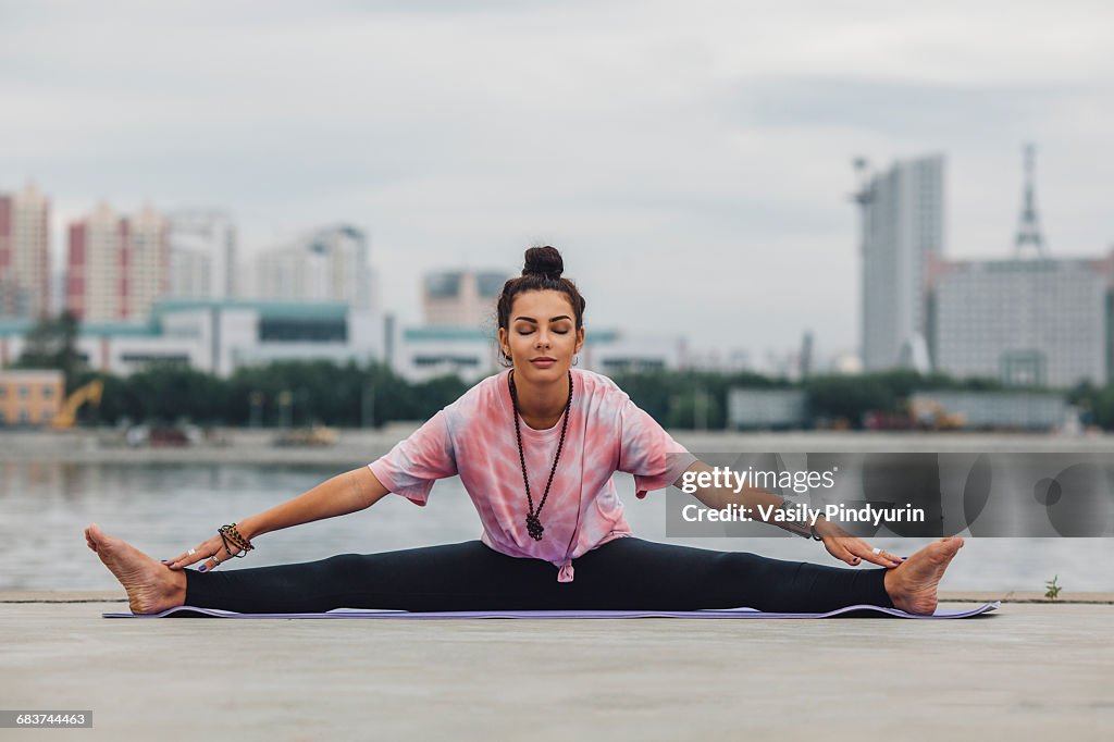 Beautiful woman practicing yoga against river in city