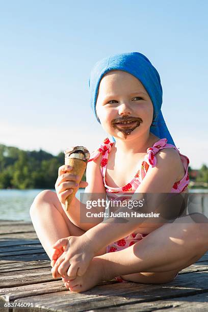 portrait of female toddler on pier eating chocolate ice cream cone, lake seeoner see, bavaria, germany - girl eating messy ice cream cone stock-fotos und bilder