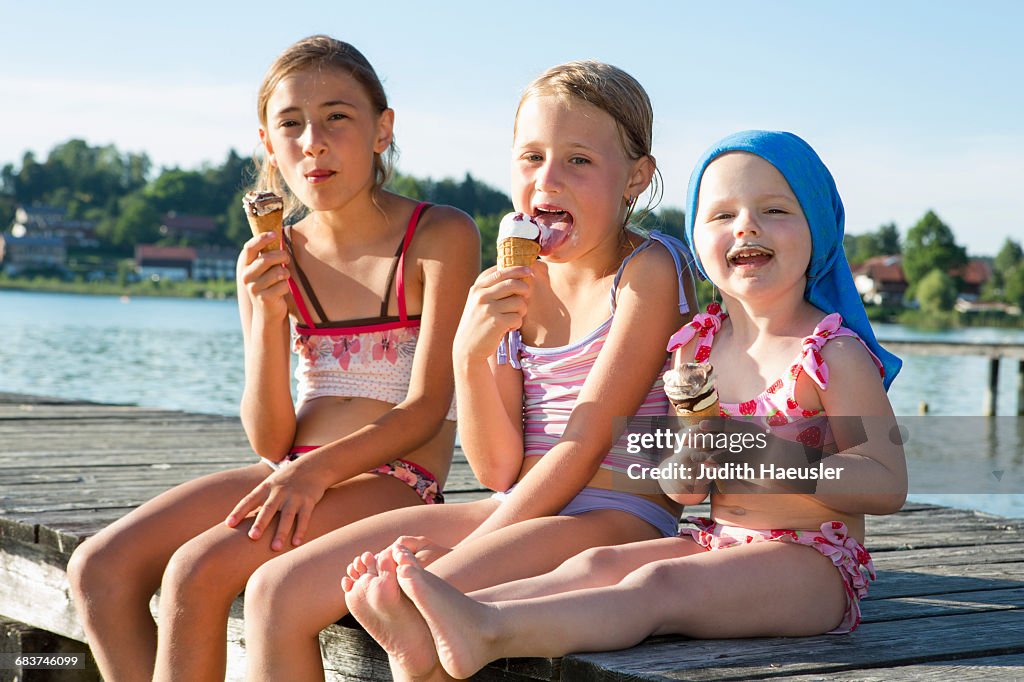 Two sisters and female toddler on pier eating ice cream cones, Lake Seeoner See, Bavaria, Germany