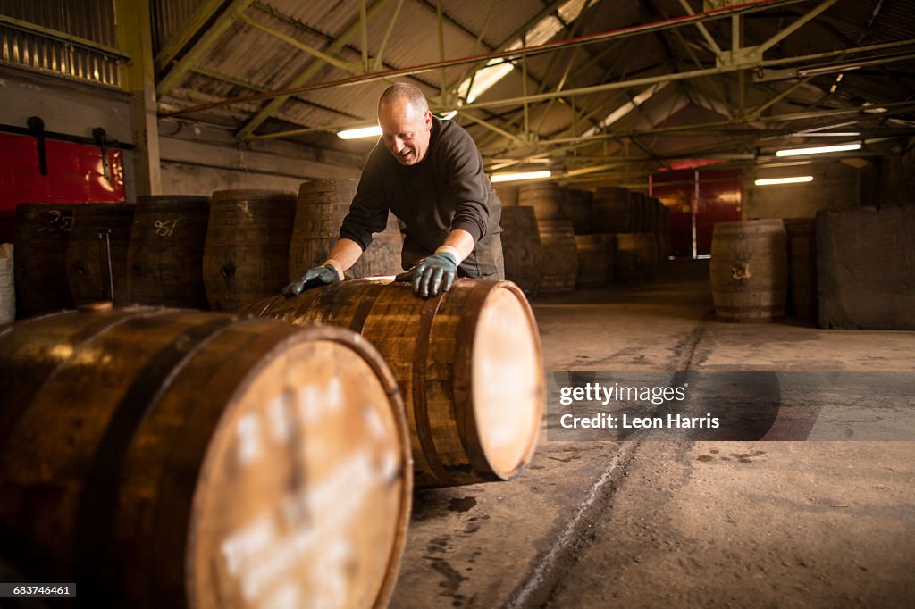 Worker rolling whisky cask in whisky distillery warehouse