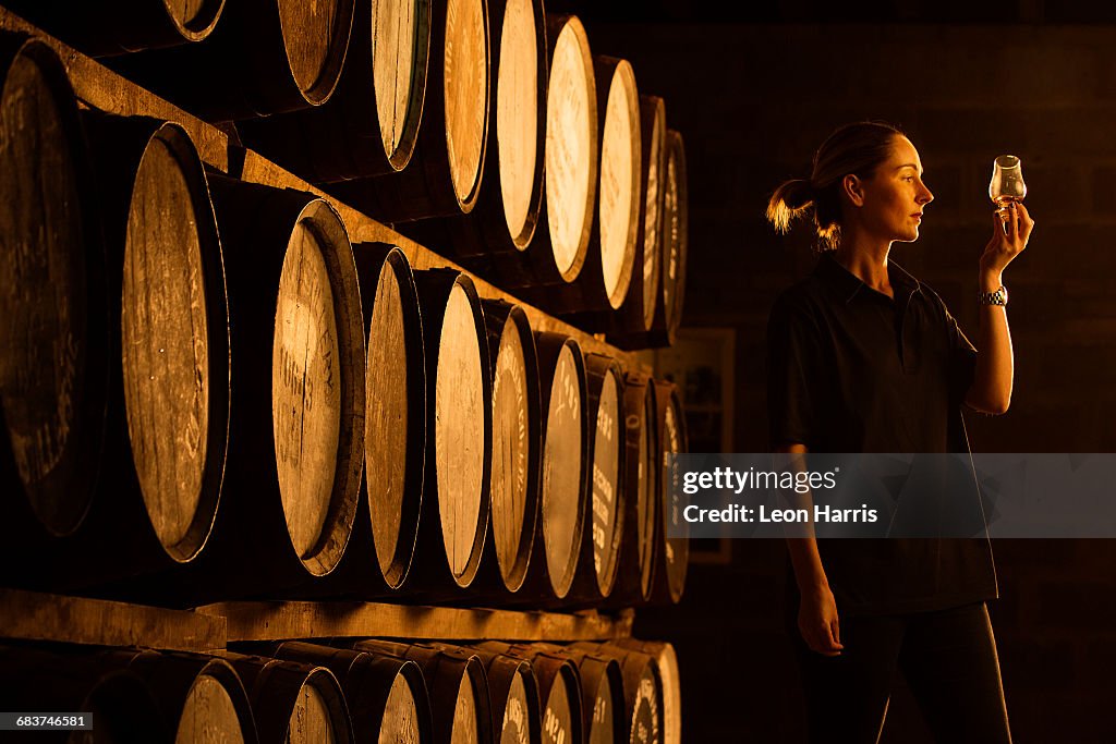 Female taster looking at the colour of whisky in glass at whisky distillery