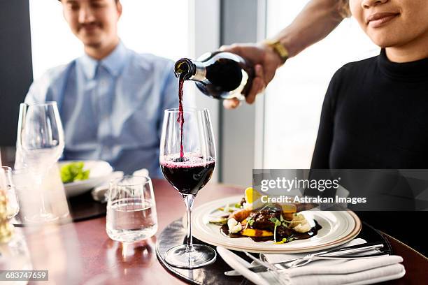 cropped image of waiter serving red wine for female customer at restaurant - gieten stockfoto's en -beelden