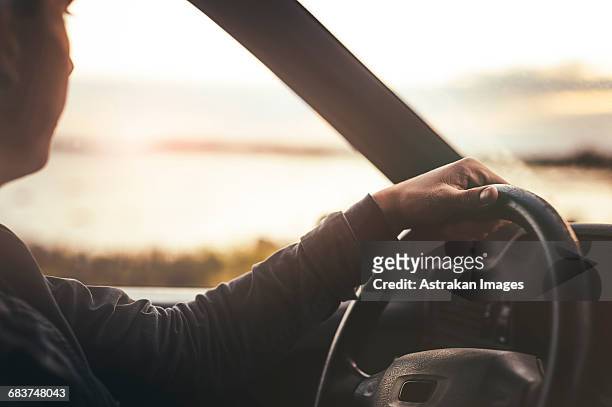 cropped image of man looking at sunset view while driving car - car interior side stock pictures, royalty-free photos & images