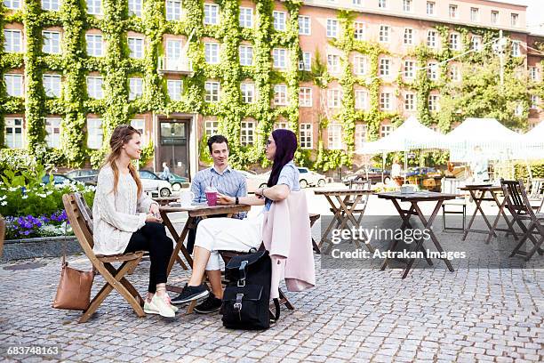friends discussing at sidewalk cafe in town square - cafe table chair outside stock pictures, royalty-free photos & images