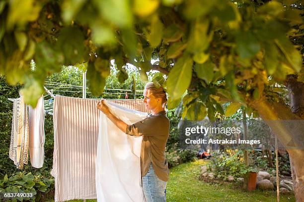 woman hanging laundry on clothesline in backyard - clothesline stock pictures, royalty-free photos & images