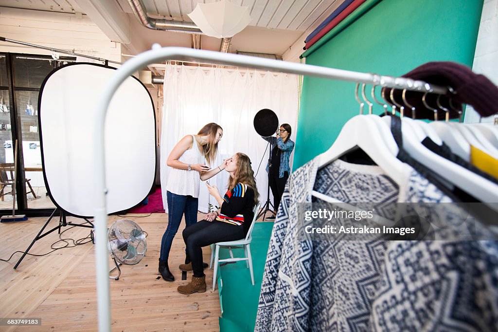 Fashion model applying make-up to sister while assistant working in studio