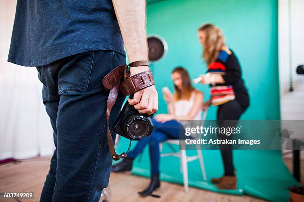 midsection of photographer holding digital camera while models getting dressed in background at studio - photo shoot makeup stock pictures, royalty-free photos & images