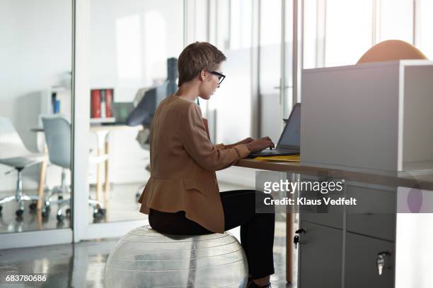 businesswoman sitting on fitness ball, at office desk - yoga ball work stock pictures, royalty-free photos & images