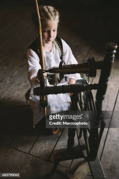 niedliche blonde kleine kind mädchen tragen tracht aus holz spinnrad in alten haus zu sitzen - spinnrad stock-fotos und bilder