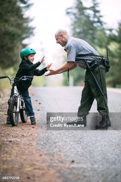 police officer talking to child on bike - police officer smiling stock pictures, royalty-free photos & images
