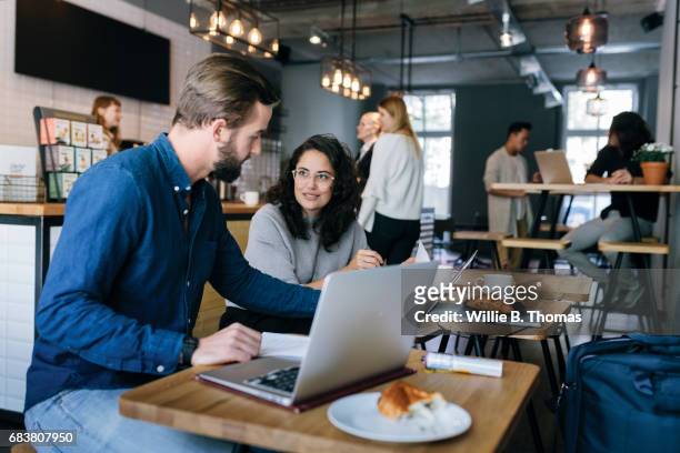Man Discussing Work With Colleague At A Busy Business Cafe