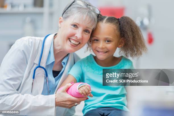 fröhliche leitender kinderarzt mit patienten - kind gips stock-fotos und bilder