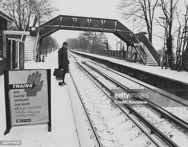 Lone commuter stands on the snow covered platform of Shoreham Station near Sevenoaks on the Southern Rail line waiting for a train that has been...