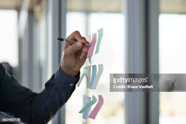 businessman writing on paper note on glass wall, in modern office space - post it note pad stock pictures, royalty-free photos & images