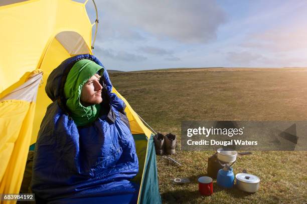 man looking out of tent with camping equipment. - sleeping bag stock pictures, royalty-free photos & images