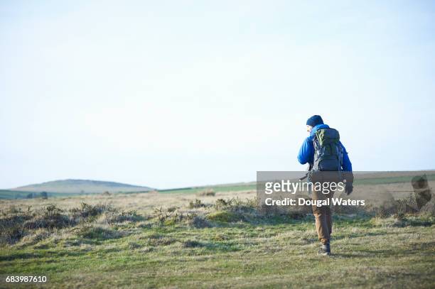 hiker with backpack walking over barren moorland. - young men camping stock pictures, royalty-free photos & images