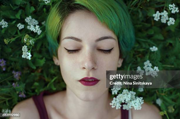 woman with green hair lays in grass with white flowers - androgynous stock-fotos und bilder