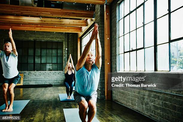 students in chair pose during class in yoga studio - 40s woman t shirt studio imagens e fotografias de stock