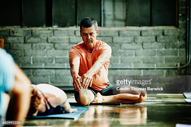 mature man in seated stretch during yoga class - senior yoga stock pictures, royalty-free photos & images