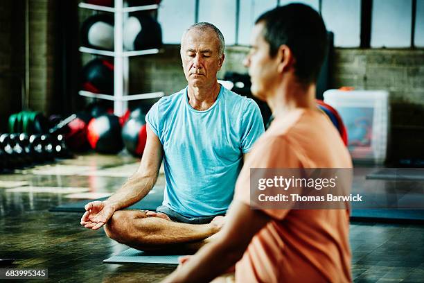 two mature men in lotus pose during class - thomas chan stock pictures, royalty-free photos & images