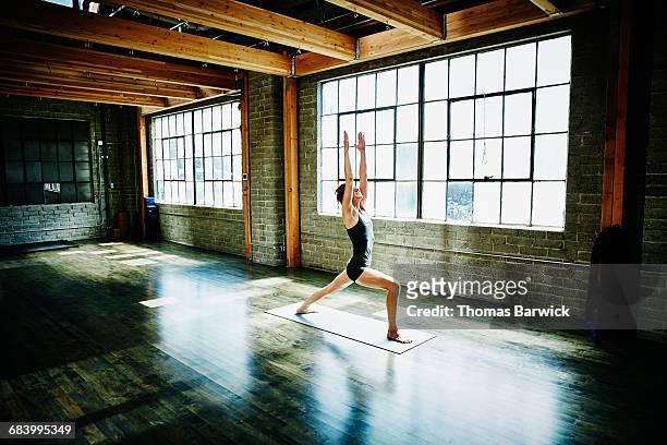 woman in warrior pose in empty yoga studio - yoga studio stock pictures, royalty-free photos & images