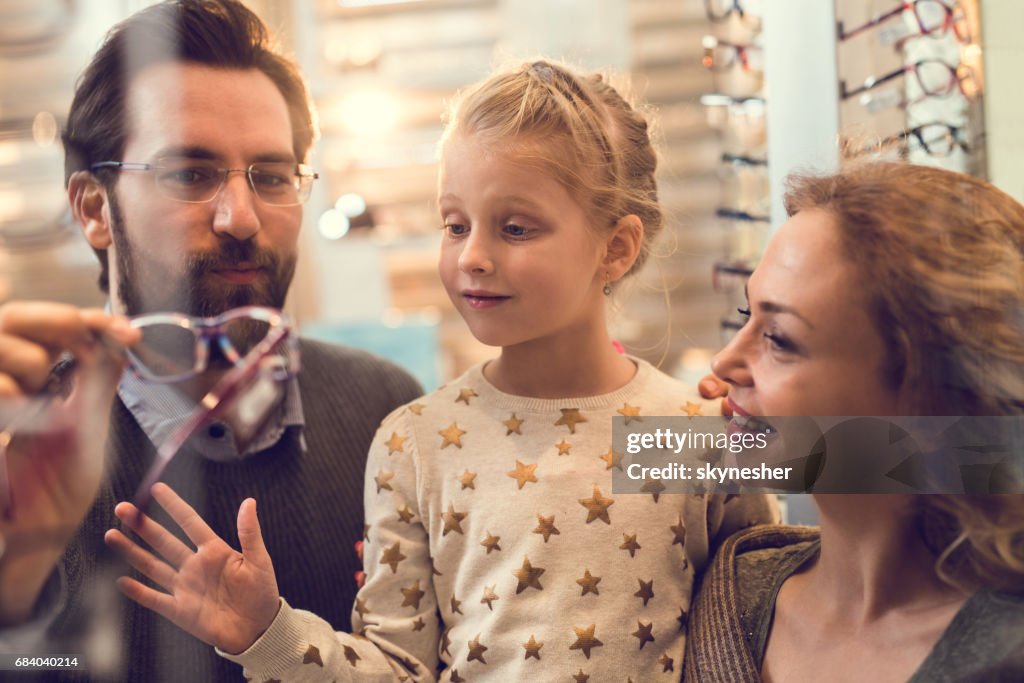 Lyckliga föräldrar att välja glasögon för deras lilla dotter på optiker butik.