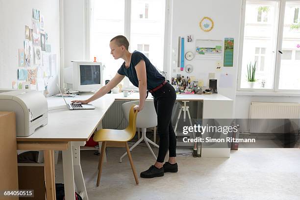 casual businesswoman using laptop in modern office - standing on chair stockfoto's en -beelden