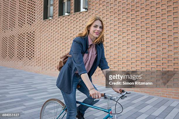 smiling young woman riding bicycle in the city - blue purse stock pictures, royalty-free photos & images