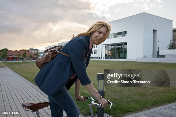 cheerful young businesswoman riding bicycle - weggucken stock-fotos und bilder
