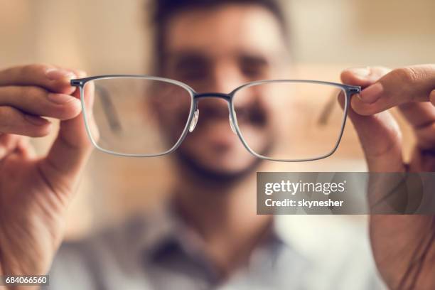 close up of a man holding eyeglasses before trying them on. - reading glasses stock pictures, royalty-free photos & images