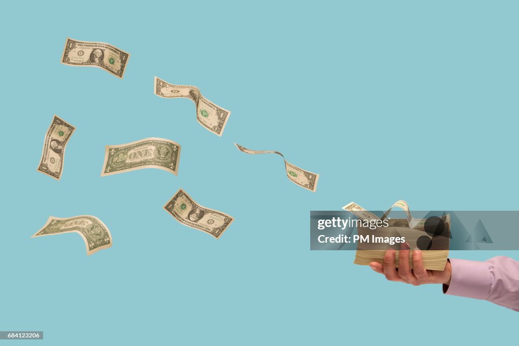 Money flying off stack of bills in man's hand