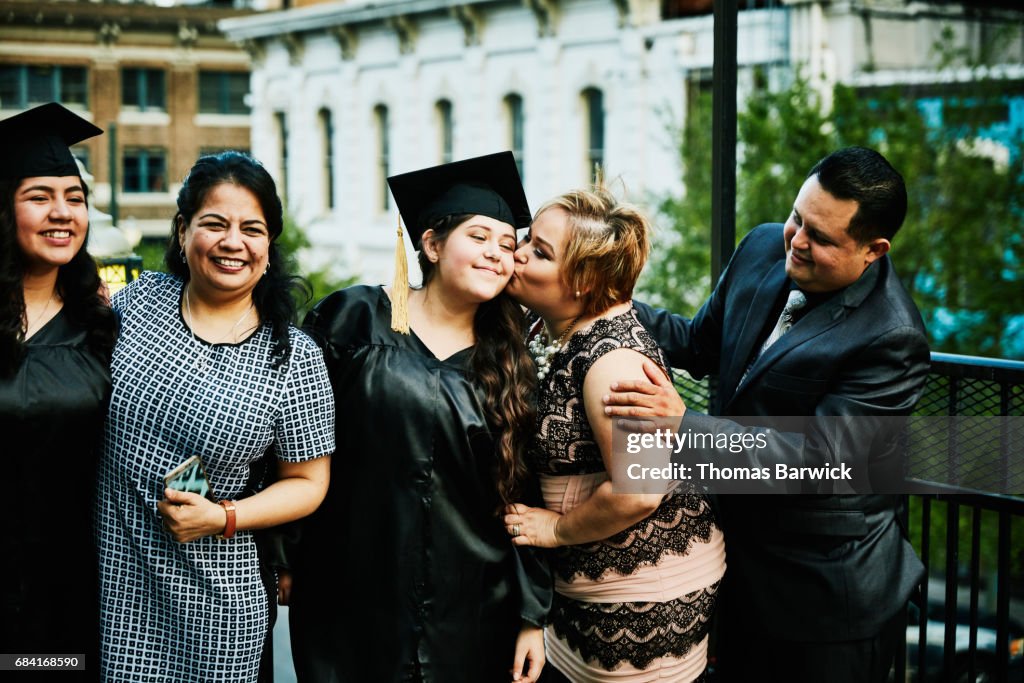 Mother kissing graduating daughter during family celebration on restaurant deck