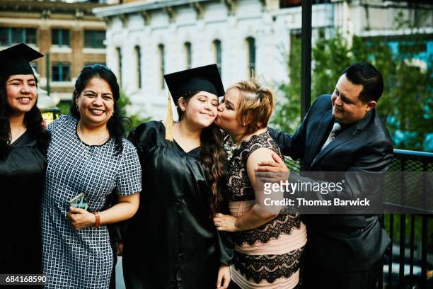 Mother kissing graduating daughter during family celebration on restaurant deck