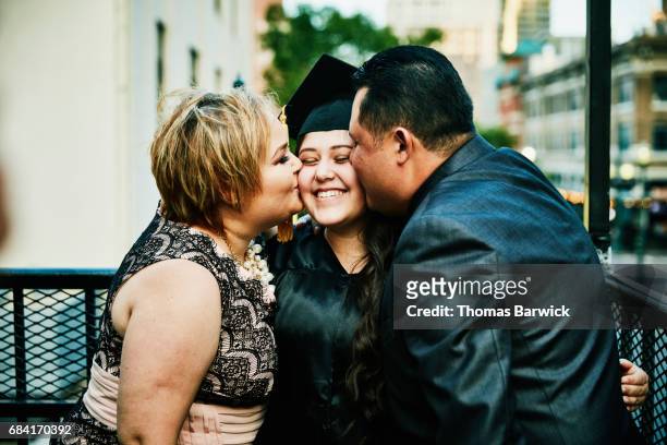 Mother and father kissing graduating daughter during family celebration
