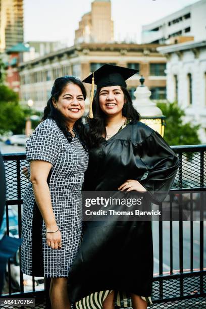 Smiling mother and daughter posing for graduation photos during celebration on restaurant deck