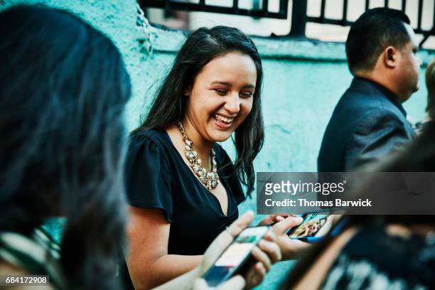 Laughing young woman showing photo on smartphone to friend during celebration dinner