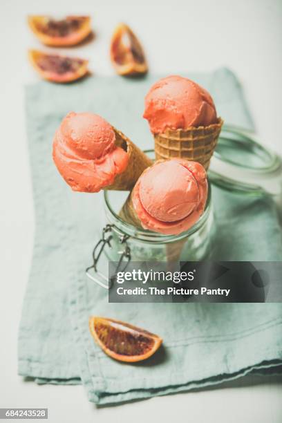 refreshing summer blood orange ice cream or sorbet scoops in sweet waffle cones in glass jar served with fresh orange slice - orange sorbet stock pictures, royalty-free photos & images